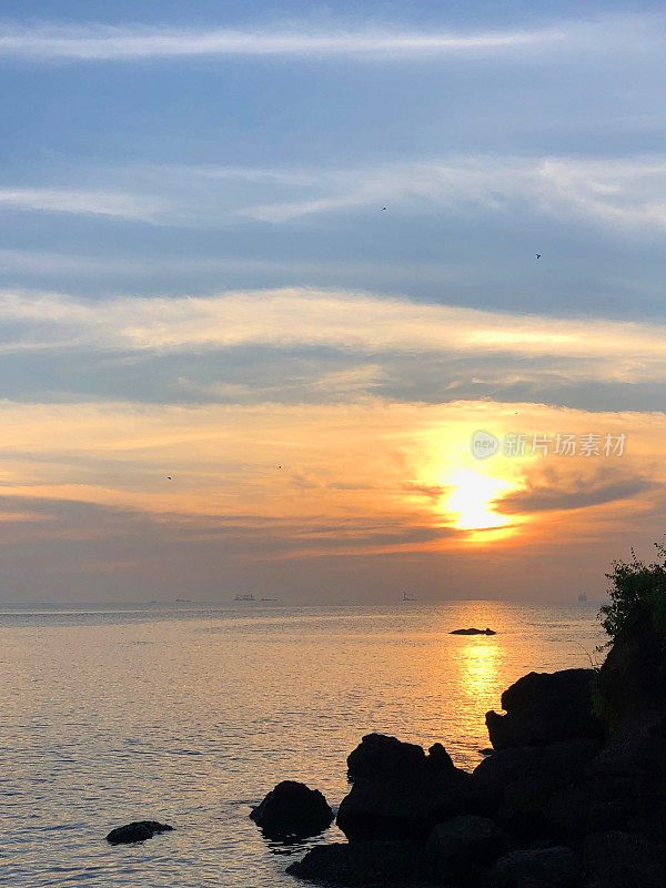 令人惊叹的印度果阿海滩的图像与橙色的日落天空，大海，云彩和日出/日落海岸线的倒影在多纳宝拉海滩照片，果阿，印度南部，岩石的剪影，沙子，涟漪拍打海岸和反射着明亮的橙色太阳